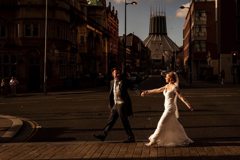 Bride and groom walk together with Metropolitan cathedral in background