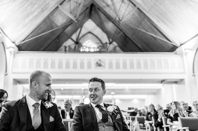 The groom and best man share a joke while waiting at the church