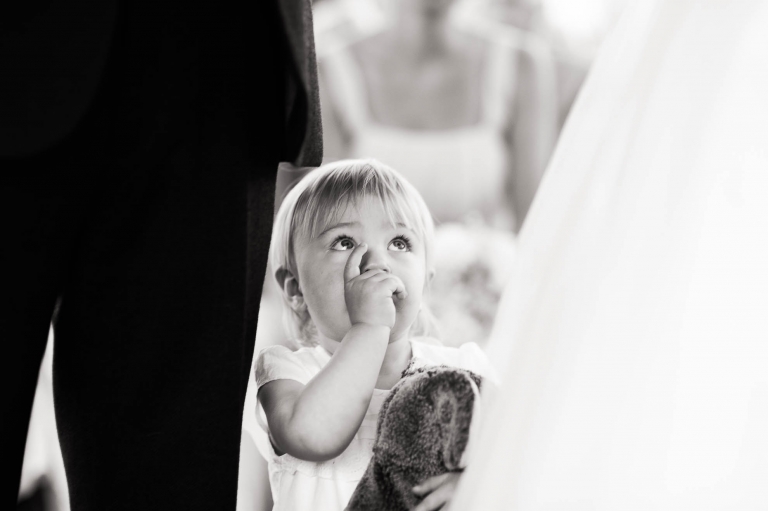 Flower girl looks up at the bride and groom during the wedding ceremony