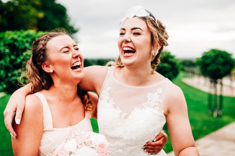 Bridesmaid and bridesmaid hold each other laughing