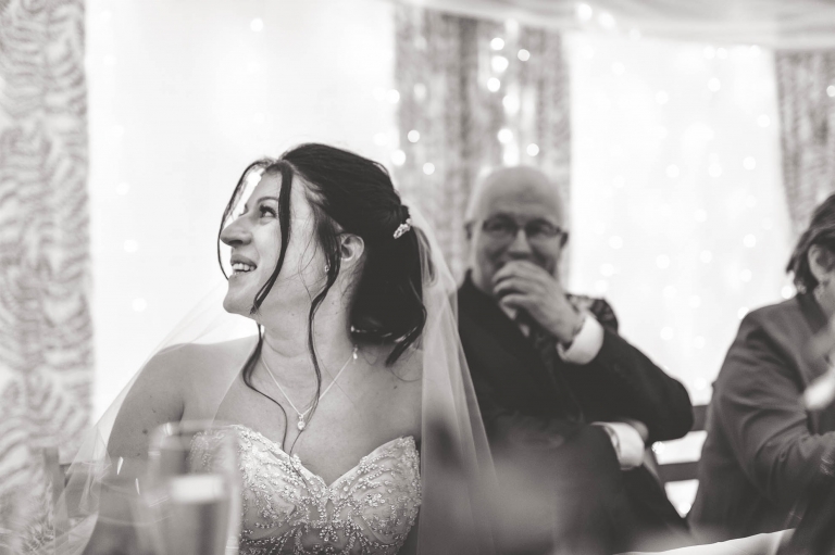 Bride smiles as the groom gives his speech