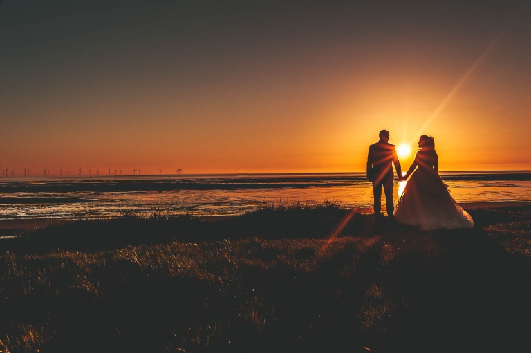 silhouette of bride and groom hold ahnds with sunset