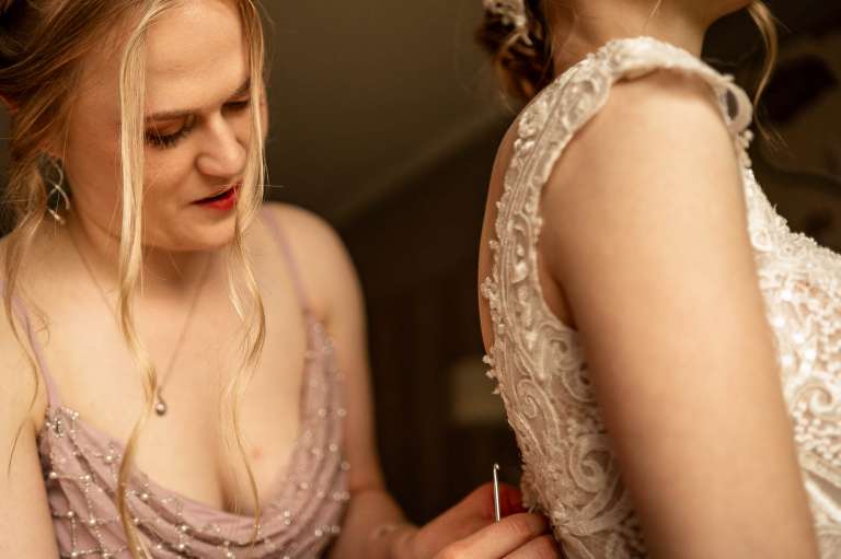 Close up of bridesmaid helping bride into her dress
