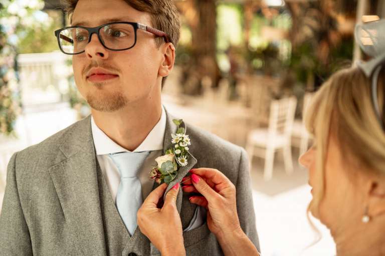 Grooms mother helps groom but on his buttonhole flower