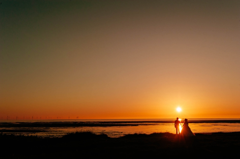 Bride and groom hold hands at sunset