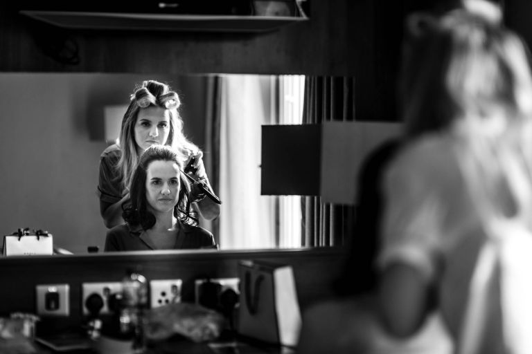 Bride looks in mirror as she has her hair done