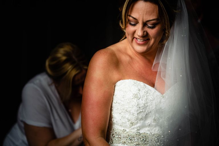 Bride smiling as she puts on her wedding dress