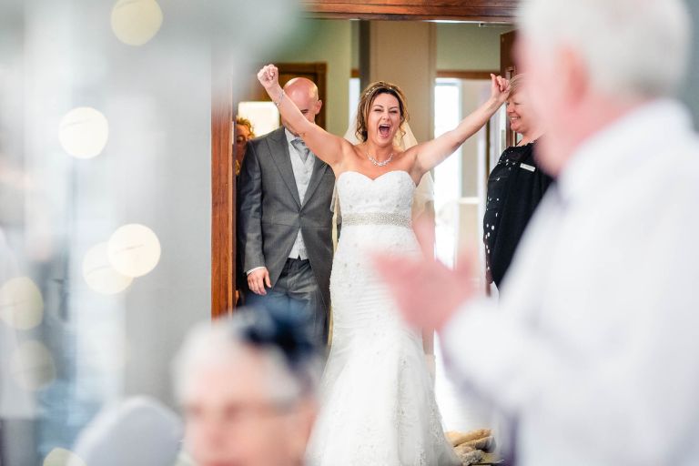 Bride puts her hands in the air as the newlyweds are announced into wedding breakfast