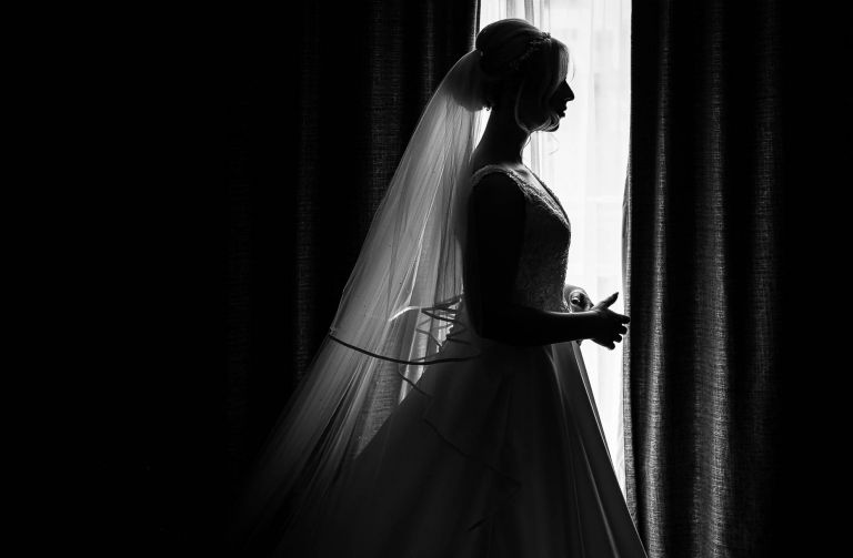 Bride stands by the window in her dress