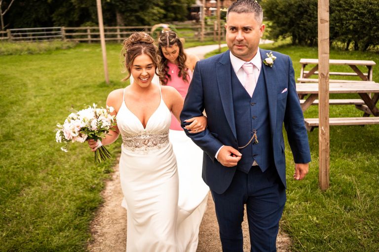 Bride walks with father of the bride and bridesmaid
