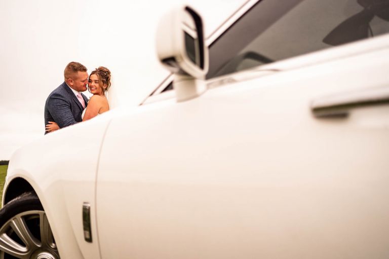 Bride and groom portrait at front of wedding car