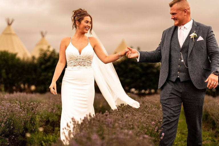 Bride and groom hold hands in lavender field