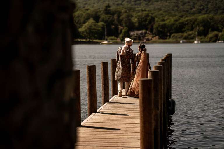 Bride and groom walk on jetty on lakeside