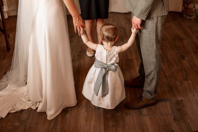 Flower girl holds bride and grooms hands during wedding ceremony